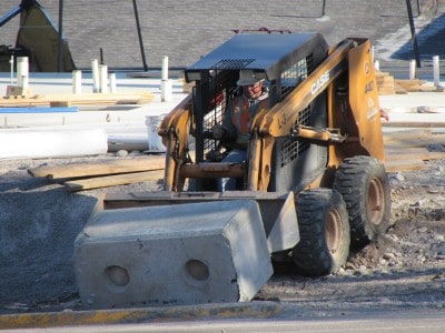 A man using a skid steer to move a cement block.